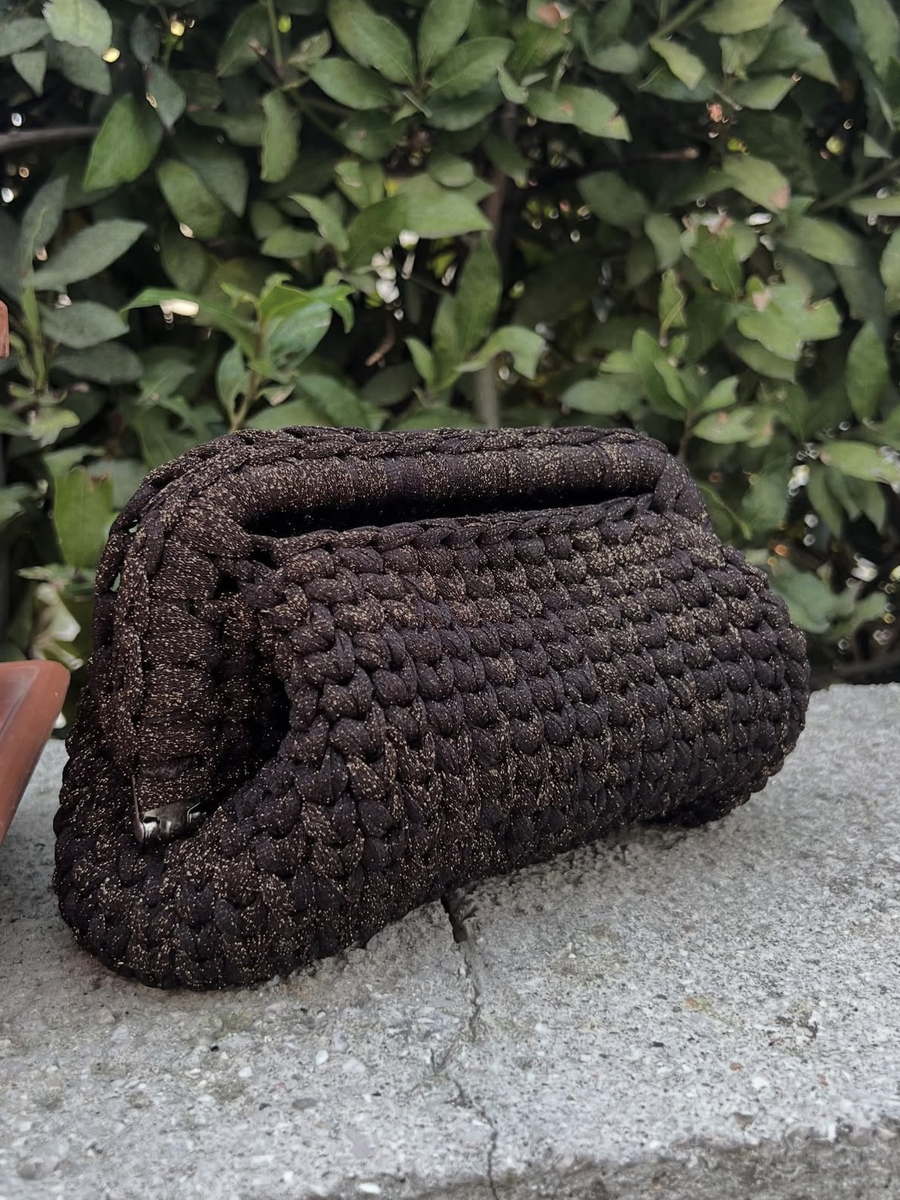 Sera: pouch in filato cioccolato attraversato da lurex dorato, appoggiata su un muretto